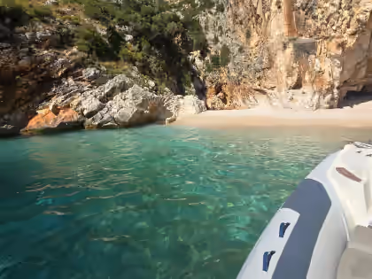 Boat approaching a clear beach cove with turquoise water near Dhërmi